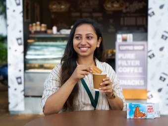A shopkeeper at her counter, holding a Milk Bikis Classic biscuit